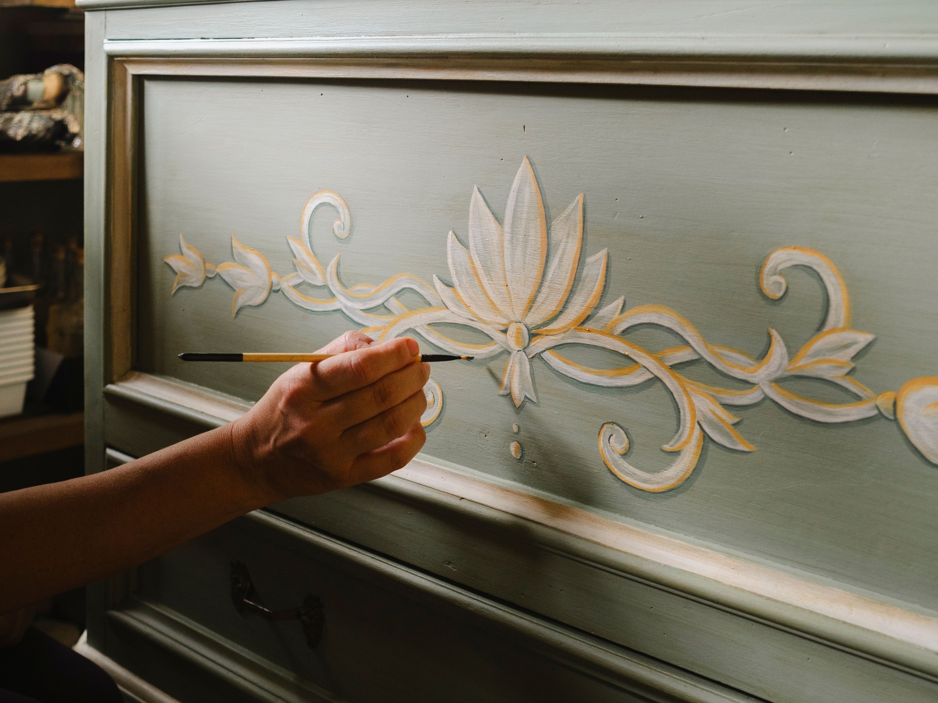 Artisan hand painting floral decoration on wooden furniture with brush